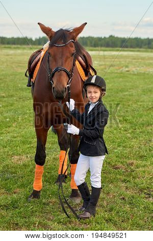 Pretty little girl jockey lead horse by its reins across country in professional outfit
