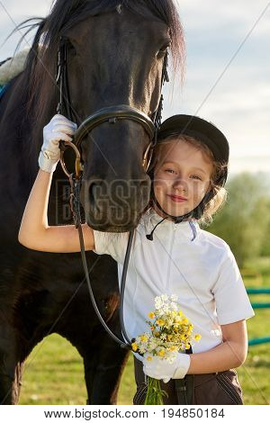 Pretty little girl jockey communicating with her black horse in professional outfit