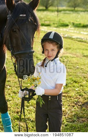 Pretty little girl jockey communicating with her black horse in professional outfit