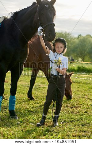 Pretty little girl jockey communicating with her black horse in professional outfit