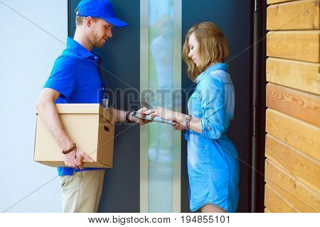Smiling delivery man in blue uniform delivering parcel box to recipient - courier service concept