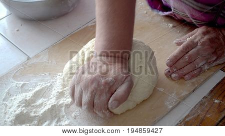 Top view shot of female hands mixing dough. Female hands knead dough on wooden board.