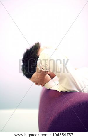 Side view of a businessman reclining on sofa with hands behind head