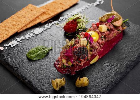 fresh beef tartar with salt and herbs and Crispbread, studio shot. Meat tartar on black shale.
