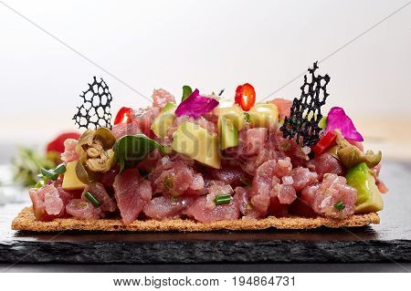 fresh tuna tartar with salt and herbs, studio shot. Fish tartar on black shale