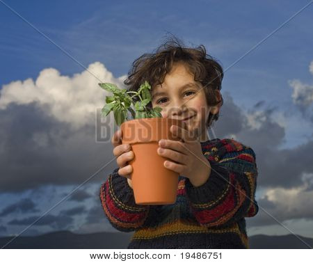 kleine jongen die een plant in een pot met wolken in de achtergrond