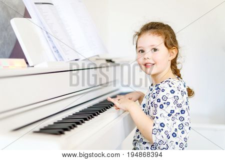 Beautiful little kid girl playing piano in living room or music school. Preschool child having fun with learning to play music instrument. Education, skills concept.