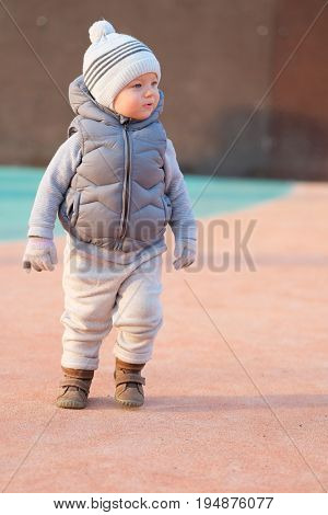 Portrait of toddler child in warm vest jacket outdoors. One year old baby boy wearing vest jacket at playground during sunset. 