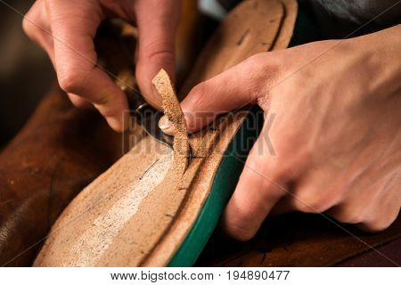 Cropped image of bootmaker sitting in workshop making shoes