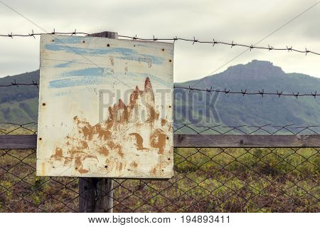 Painted sign on the fence of barbed wire and a grass field on the background of the mountains.