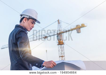 The architect wear white safety helmet and verify the blueprint with commitment on construction site with crane background