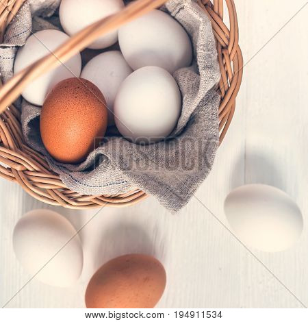 Basket with white and brown natural eggs on white wooden background.