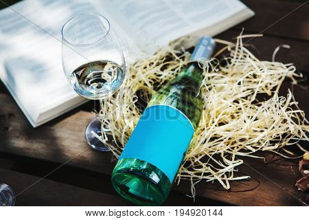 Glasswine with white wine, bottle on sawdust near big open book, romantic background with expensive alcoholic drink