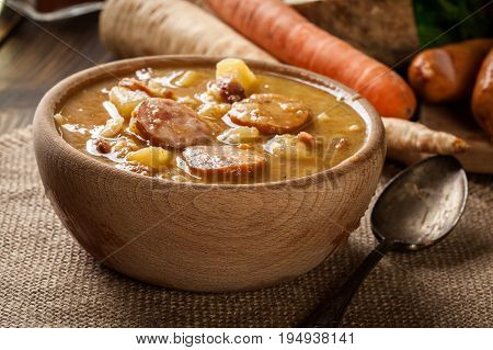 Wooden Bowl Of Split Pea Soup With Sausage And Potatoes