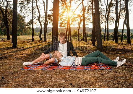 happiness of the couple sitting on a bedspread in the woods in the sunset looking at each other