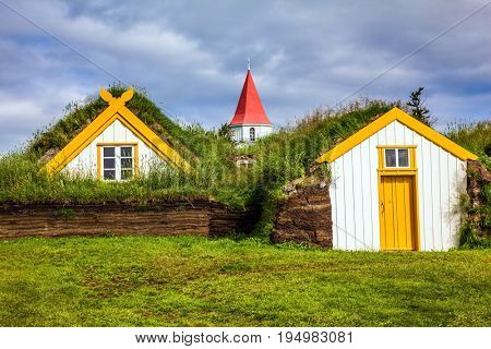 Church bell tower with gabled red roof. The old village of  houses covered with turf. Ethnographic Museum-estate Glaumbaer, Iceland. The concept of the historical and cultural tourism