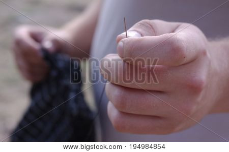 Needle with thread in the man's hand .