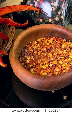 Red chili peppers and wooden bowl of chili flakes on black vertical background with reflection and copy space