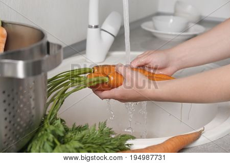 Woman washing fresh carrots in kitchen sink