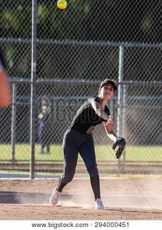 Female Teenage Softball Player In Black Uniform Throwing Ball Across Infield For The Out In A Cloud 