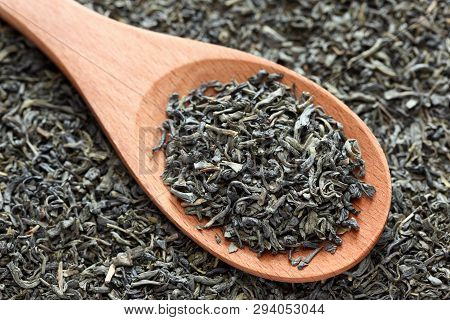 Dried Green Tea Leaves On A Wooden Spoon On A Dried Green Tea Leaves Background. Close-up.