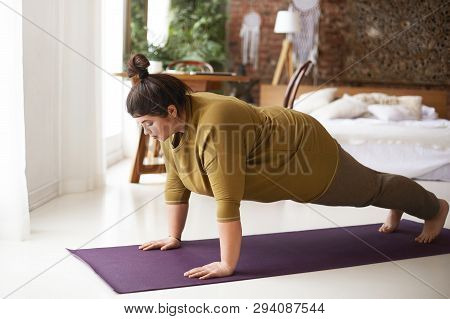 Health, Fitness And Sports Concept. Plus Size Young Brunette Woman Doing Plank Exercise On Mat In Co