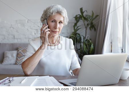 Indoor Image Of Attractive Senior Female Real Estate Agent With Short Gray Hair Sitting At Desk In F