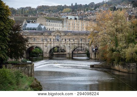 A View From Down River Of Pultney Bridge And Weir With Houses Of Bath Rising Behind