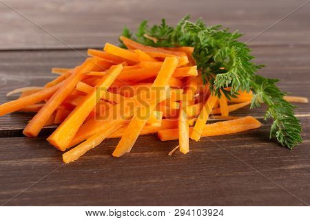 Lot Of Pieces Of Fresh Orange Carrot Cut Into Thin Noodles With Greens On Brown Wood