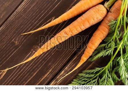 Group Of Three Whole Fresh Orange Carrot With Greens Flatlay On Brown Wood