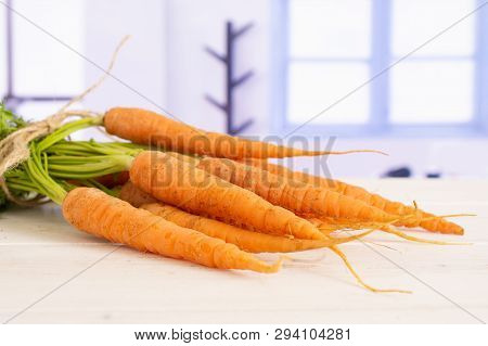 Lot Of Whole Fresh Orange Carrot Bunch With Greens Tied By Jute With Blue Window In A White Kitchen