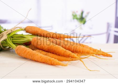 Lot Of Whole Fresh Orange Carrot Bunch With Greens Tied By Jute With Red Flowers On White In Backgro