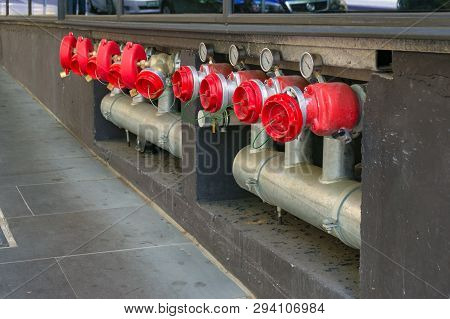 Bright Hydrant Boosters In A Row With Metal Pipes And Red Caps. Industrial Urban Infrastructure