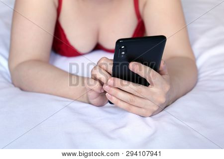 Sexy Woman In Red Bra Lying On The Bed And Using Smartphone. Mobile Phone In Female Hands, Concept O