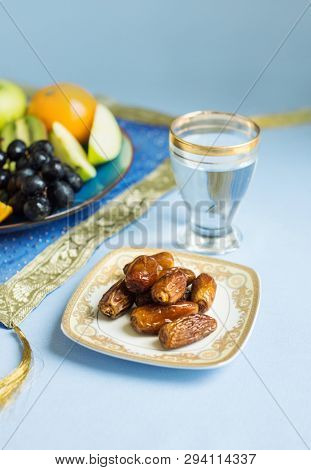 Wholesome, healthy and fat-free food consists of assorted fruits and sweet dates while breaking Ramadan fast. Glass of pure drinking water and dates with fruit plater for Iftar ritual.