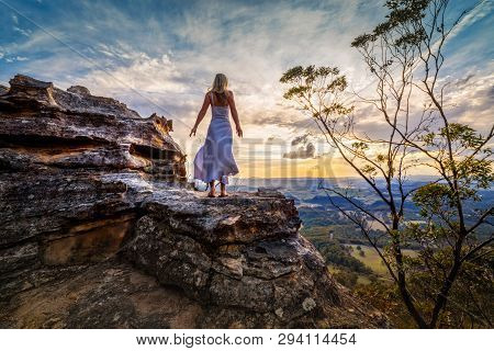 Standing On A Rocky Ledge With Valley Views And Distant Mountains, Dress Blowing In The Wind She Dre