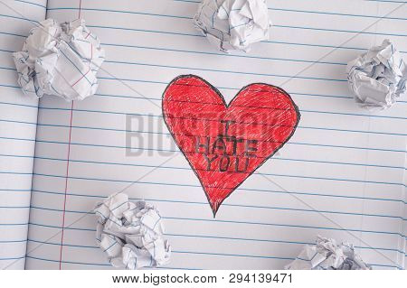 I Hate You. Red Heart With Phrase I Hate You On Notebook Sheet With Some Crumpled Paper Balls On It.