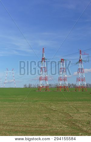 Supports Power Lines Are In The Field. Red And White Against A Bright Blue Sky. New Line
