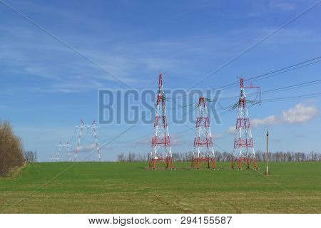 Supports Power Lines Are In The Field. Red And White Against The Blue Sky. New Line