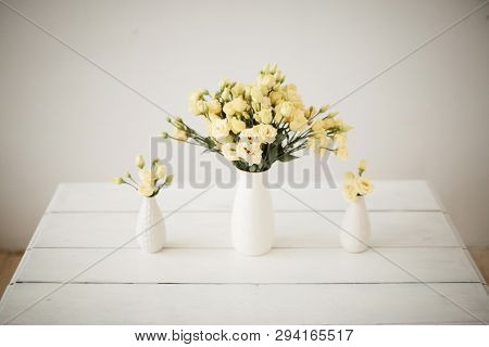Three Bouquets With Yellow Flowers Stand On A Wooden Table On A Light Background In White Vases