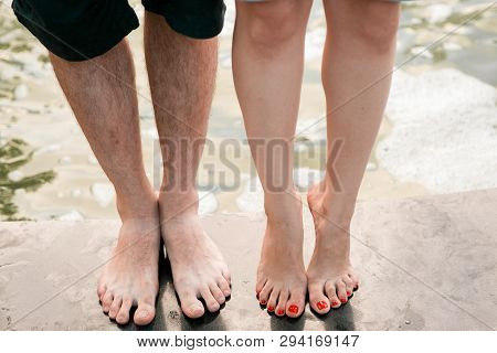Male And Female Barefoot Pairs Of Feet Are Standing On Wet Gray Asphalt