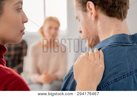 Young female keeping her hand on shoulder of sad groupmate while expressing empathy and care