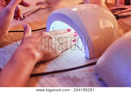 Client With Red Varnish At Manicure Salon Dryes Gel Polished Nails In Uv Light. Closeup Shoot.