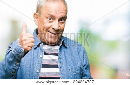 Handsome senior man wearing denim jacket doing happy thumbs up gesture with hand. Approving expression looking at the camera with showing success.