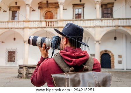 Man With Professiona Camera And Hat With Backpack Stay In Yard Of A Castle. Poland