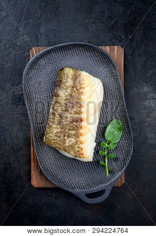 Fried Japanese skrei cod fish filet with wasabi lettuce as top view on a modern design plate 