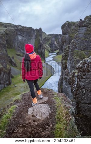 A Girl In A Red Jacket Stands On The Edge Of A Deep Gorge. A Mountain River Flows Into The Gorge. Pi