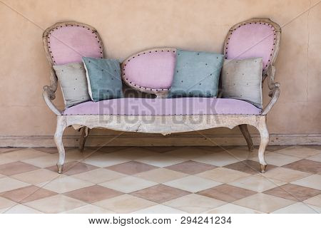 Pink Textile Vintage Style Sofa With Blue And Gray Pillows Near Peachy Background. Interior Concept.