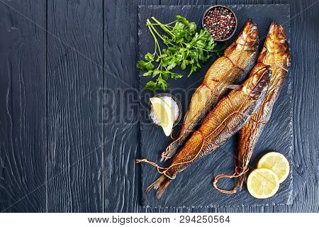Hot Smoked Whole Herrings With Lemon Slices, Parsley And Peppercorns On A Black Slate Tray  On A Woo