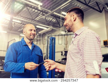 auto service, repair, maintenance and people concept - mechanic with clipboard giving key to happy smiling man or owner at car shop